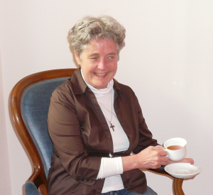 B. Seeholzer mit einer Teetasse in der Hand auf einem Stuhl sitzend